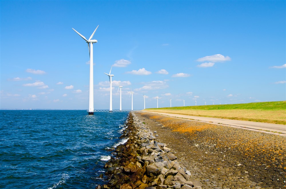 Wind energy windmills near highway and sea shore. 