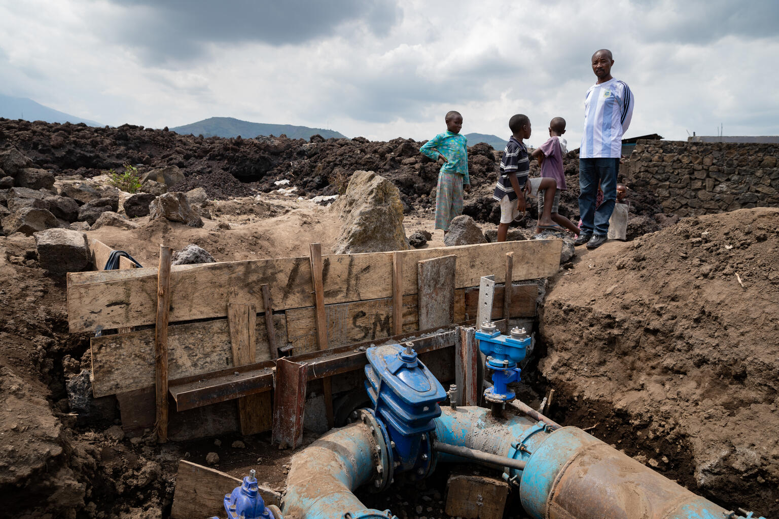 A resident, surrounded by his children, looks at one of the main pipes that supplies water to the city of Goma, North Kivu, DRC. which was damaged by the volcanic eruption. The sudden eruption of the Nyiragongo volcano on the evening of 22 May 2021, generated two lava flows towards the city of Goma in the east of the Democratic Republic of Congo. Thousands of people fled the town of Goma city and many moved for the village of Sake. One of the major problems following this event is access to drinking water f A resident, surrounded by his children, looks at one of the main pipes that supplies water to the city of Goma, North Kivu, DRC. which was damaged by the volcanic eruption. The sudden eruption of the Nyiragongo volcano on the evening of 22 May 2021, generated two lava flows towards the city of Goma in the east of the Democratic Republic of Congo. Thousands of people fled the town of Goma city and many moved for the village of Sake. One of the major problems following this event is access to drinking water f