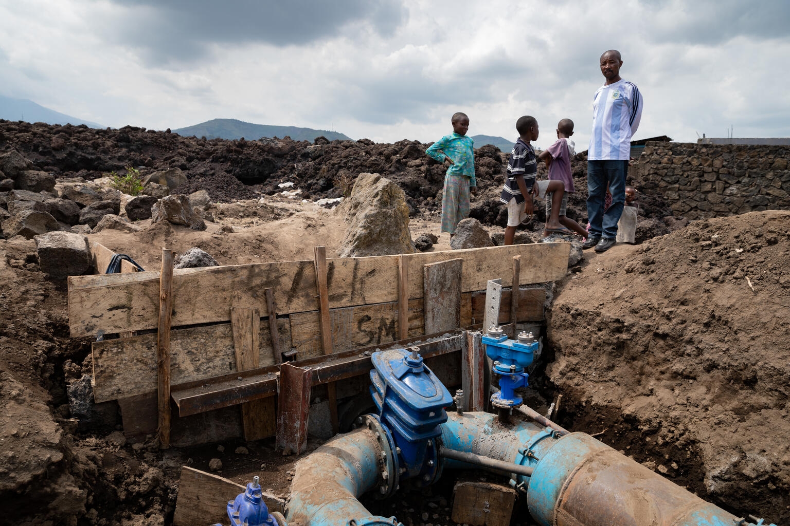 A resident, surrounded by his children, looks at one of the main pipes that supplies water to the city of Goma, North Kivu, DRC. which was damaged by the volcanic eruption. The sudden eruption of the Nyiragongo volcano on the evening of 22 May 2021, generated two lava flows towards the city of Goma in the east of the Democratic Republic of Congo. Thousands of people fled the town of Goma city and many moved for the village of Sake. One of the major problems following this event is access to drinking water f A resident, surrounded by his children, looks at one of the main pipes that supplies water to the city of Goma, North Kivu, DRC. which was damaged by the volcanic eruption. The sudden eruption of the Nyiragongo volcano on the evening of 22 May 2021, generated two lava flows towards the city of Goma in the east of the Democratic Republic of Congo. Thousands of people fled the town of Goma city and many moved for the village of Sake. One of the major problems following this event is access to drinking water f